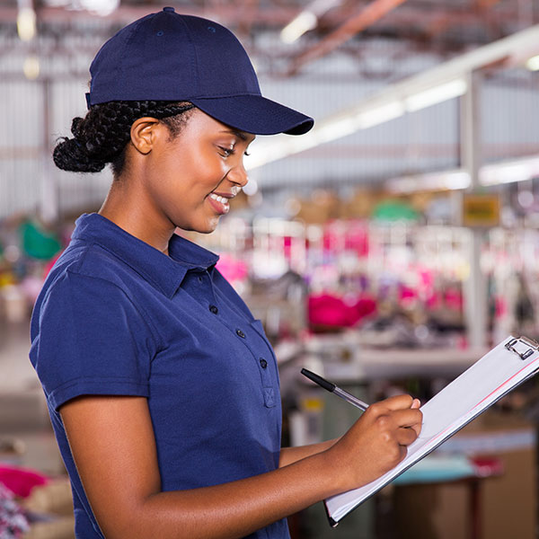 A female warehouse worker smiling while writing on a clipboard